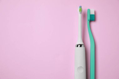 Pembe arka planda elektrikli ve plastik diş fırçaları. Metin için boşluk