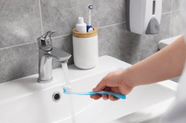 Banyodaki musluktan akan suyun altında plastik diş fırçası yıkayan kadın, yakın plan.