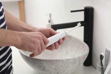 Banyoda elektrikli diş fırçası tutan adam lavabonun üstünde, yakın plan.