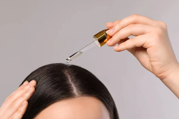 stock image Woman applying essential oil onto hair roots on light grey background, closeup