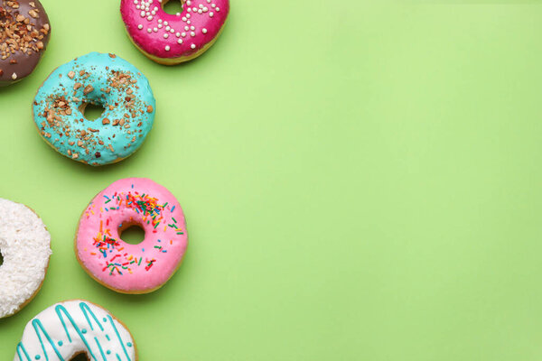 Different tasty glazed donuts on green background, flat lay. Space for text