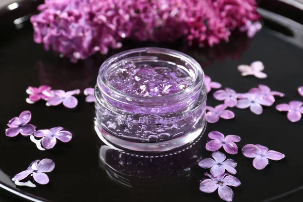 Jar of cosmetic product and lilac flowers on black surface