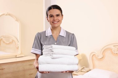 Genç oda hizmetçisi otel odasında bir yığın temiz havlu tutuyor.