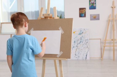 Stüdyoda resim yapan küçük bir çocuk. Tuvali tutmak için resim sehpası kullanılıyor