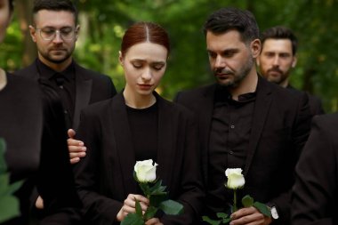 Cenaze töreni. Beyaz gül çiçekleri olan üzgün insanlar dışarıda yas tutuyorlar.