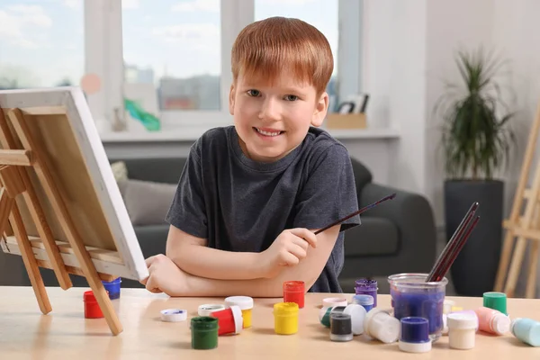 スタジオでテーブルで絵を描く幸せな少年 イーゼルを使用してキャンバスを保持する — ストック写真