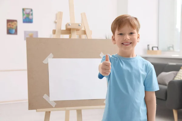 スタジオで親指を見せてくれる 幸せな少年 イーゼルを使用してキャンバスを保持する — ストック写真