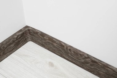 Beyaz duvarın yanında, kaplamalı zeminde konnektörlü siyah ahşap kaide.