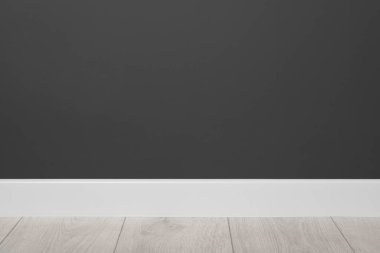 Siyah duvarın yanında, kaplamalı zeminde beyaz bir kamış var.