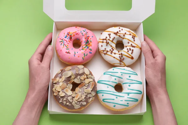 stock image Woman holding box with tasty glazed donuts on light green background, top view