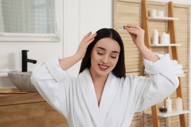 Mutlu genç bir kadın tuvaletteki saç köklerine gerekli yağı sürüyor.