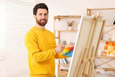 Stüdyoda resim yapan adam. Tuvali tutmak için resim sehpası kullanılıyor