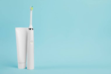 Açık mavi arkaplanda elektrikli diş fırçası ve diş macunu, metin için boşluk