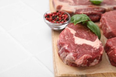 Cut fresh beef meat, spices and basil leaves on white tiled table, closeup. Space for text