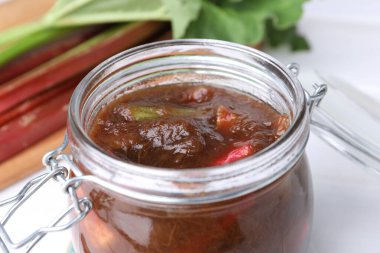 Jar of tasty rhubarb jam on white table, closeup