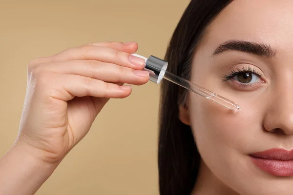 stock image Young woman applying essential oil onto face on beige background, closeup