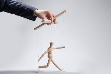 Woman pulling strings of puppet on light grey background, closeup. Space for text