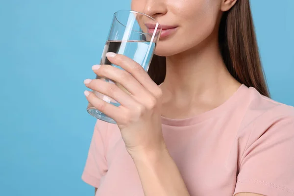 Healthy habit. Woman drinking fresh water from glass on light blue background, closeup