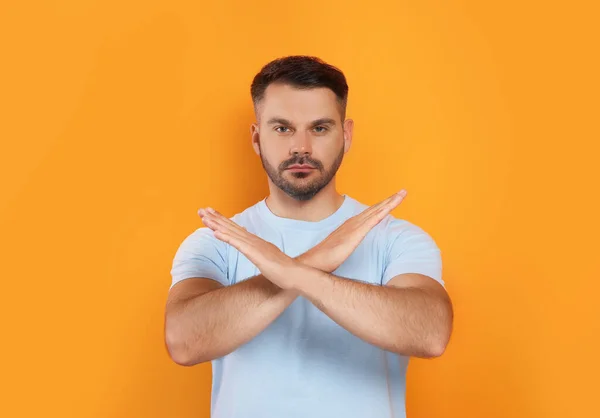 Handsome man with crossed hands on orange background. Stop gesture