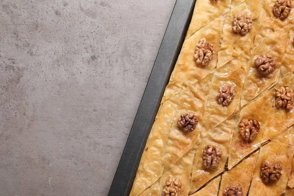 Delicious baklava with walnuts in baking pan on grey textured table, top view. Space for text