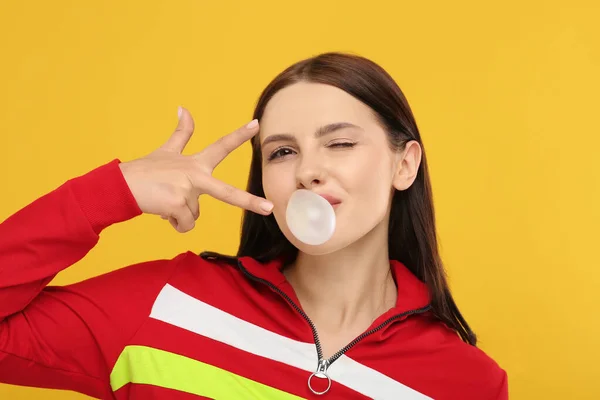 Beautiful woman blowing bubble gum and gesturing on orange background