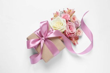 Gift box and beautiful flowers on white background, flat lay