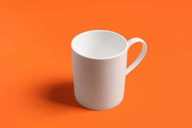 Turuncu arka planda beyaz bir seramik bardak.