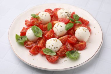 Domatesli Caprese salatası, mozzarella topları ve beyaz fayanslı fesleğen, yakın plan.