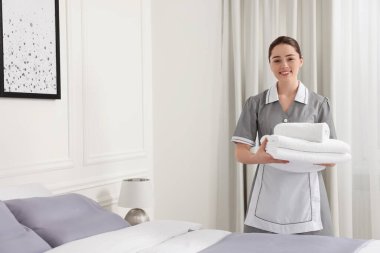 Otel odasında yatağın yanında havlu yığını olan genç bir hizmetçi. Metin için boşluk