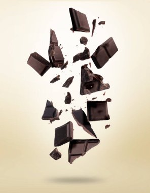 Kırık çikolata parçaları bej arka plana düşüyor.