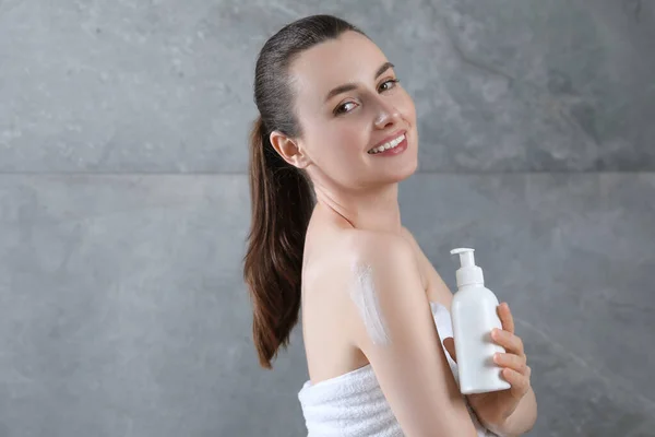 Happy woman with bottle of body cream near grey wall, space for text