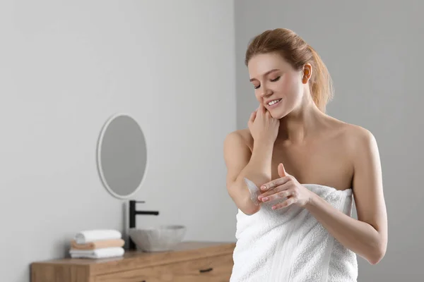 Happy woman applying body cream onto elbow in bathroom, space for text