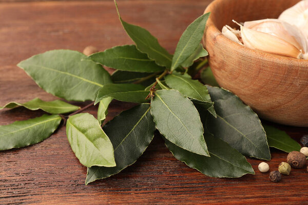 Aromatic fresh bay leaves and spices on wooden table, closeup