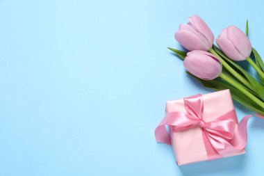 Açık mavi arka planda fiyonklu ve laleli güzel bir hediye kutusu var. Metin için boşluk