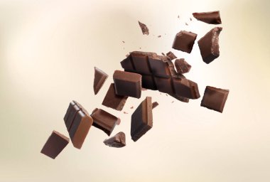 Kırık çikolata parçaları bej arka plana düşüyor.