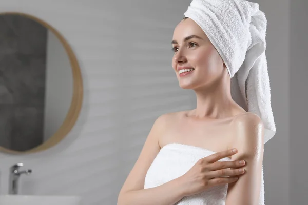 Happy woman applying body oil onto arm in bathroom, space for text