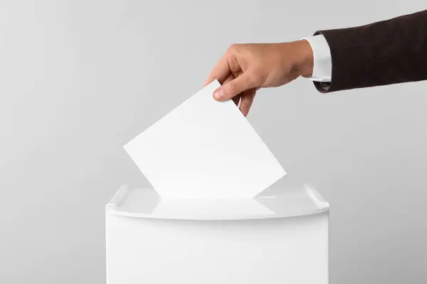 stock image Man putting his vote into ballot box on light grey background, closeup