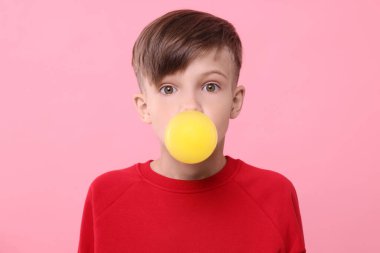 Şaşkın çocuk pembe arka planda sakız üflüyor.