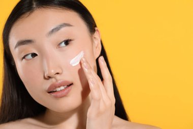 Yüzünde turuncu arka planda güneş kremi olan güzel bir genç kadın, yakın plan. Metin için boşluk