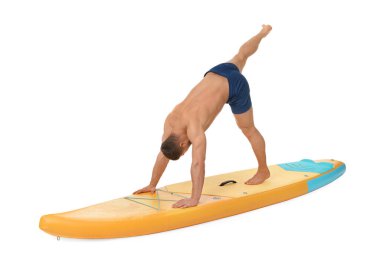Beyaz arka planda turuncu SUP tahtasında yoga yapan yakışıklı bir adam.