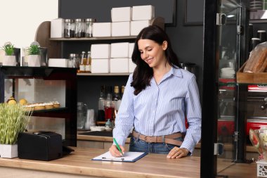 Dükkan sahibi kafesindeki panoya notlar yazıyor.