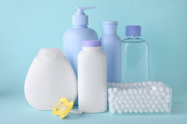 Bebek için farklı cilt bakım ürünleri, pamuk tomurcukları ve turkuaz arka planda emzik. Metin için boşluk