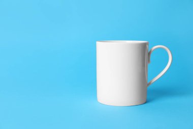 Açık mavi arka planda beyaz bir seramik bardak. Metin için boşluk