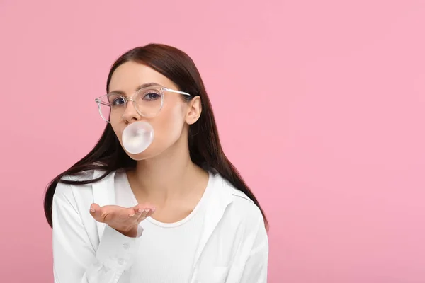 Beautiful woman blowing bubble gum on pink background, space for text