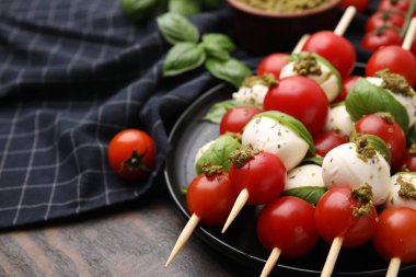 Domatesli Caprese şişleri, mozzarella topları, fesleğen ve pesto sosu ahşap masada, yakın plan. Metin için boşluk
