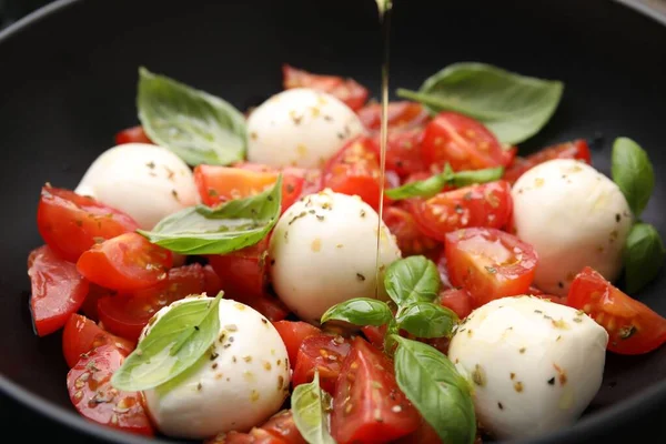 Lezzetli salata Caprese 'nin üzerine domatesli, mozzarella toplu ve fesleğenli yağ dök.