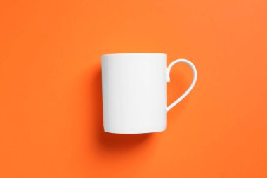 Turuncu arka planda beyaz bir seramik bardak.