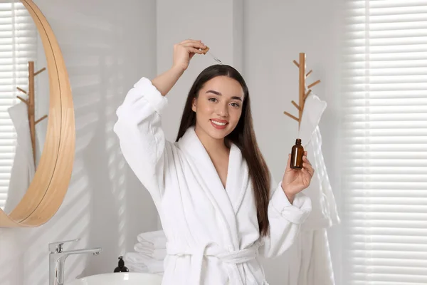 幸せな若い女性適用エッセンシャルオイルに髪の根でバスルーム — ストック写真