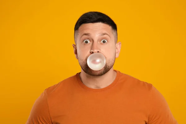 Surprised man blowing bubble gum on orange background