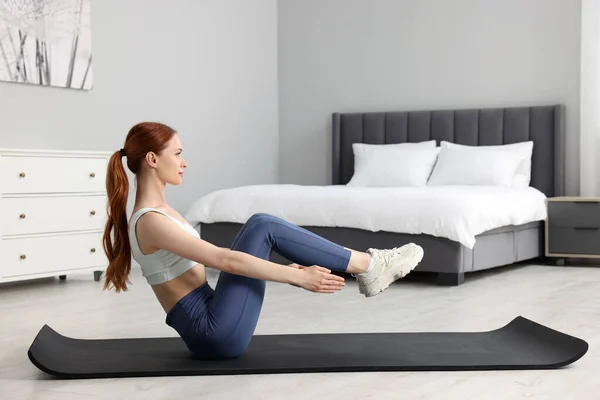 穿着运动服的年轻女子在卧室的健身垫上做运动 — 图库照片